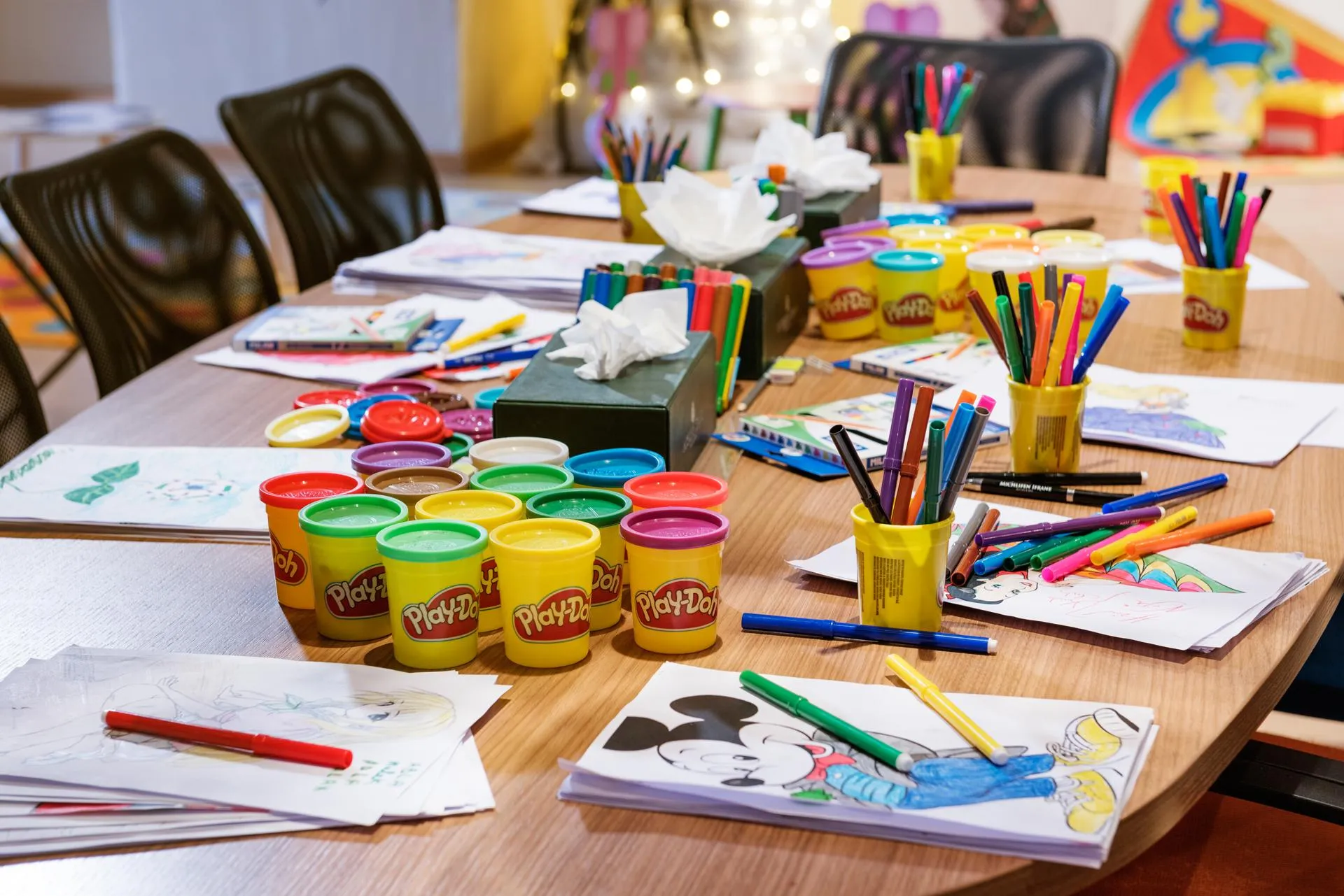 Table with drawing materials, Play-Doh clay pots, and colored sheets