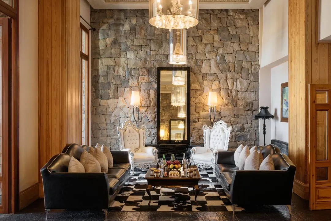 Living room with black sofas, white armchairs, coffee table, and stone fireplace, lit by lamps and a chandelier.