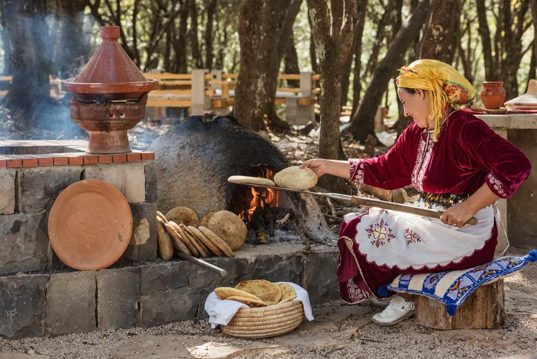 A woman in traditional attire cooks flatbreads over an outdoor wood fire.