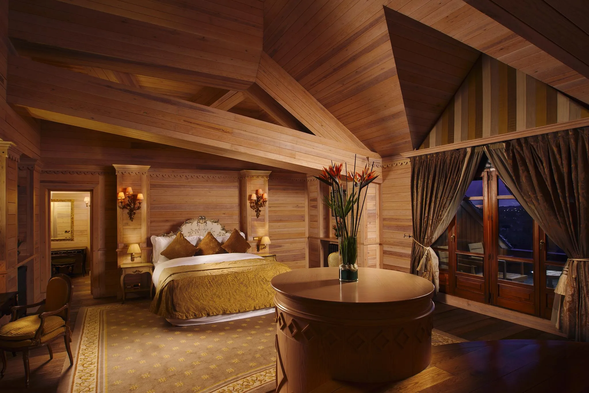 Wooden room with a four-poster bed, a round table, and windows with curtains.