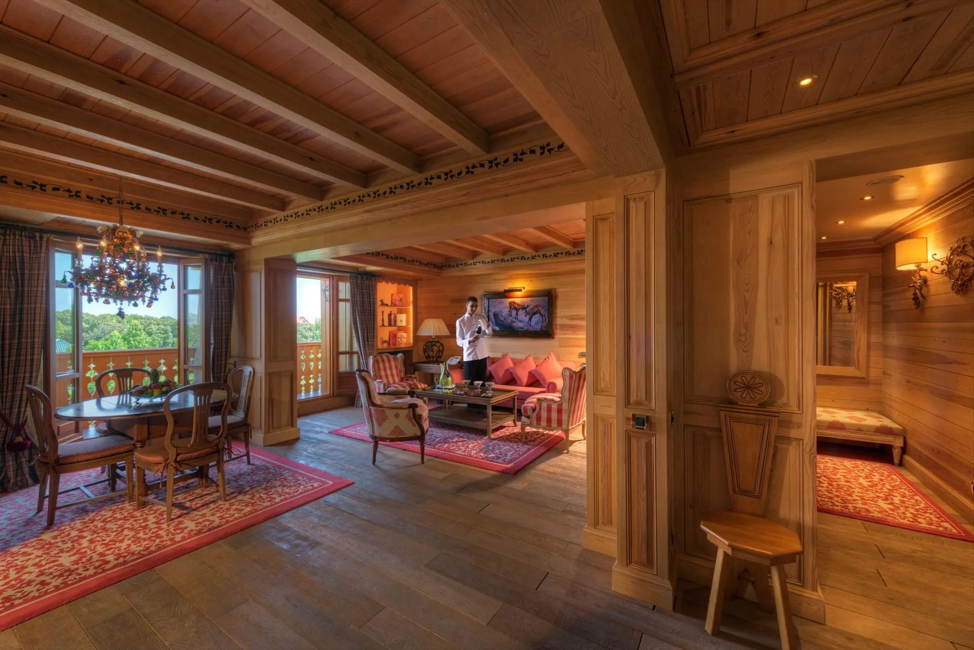 Wooden interior with living room, dining table, and a person standing near a fireplace.