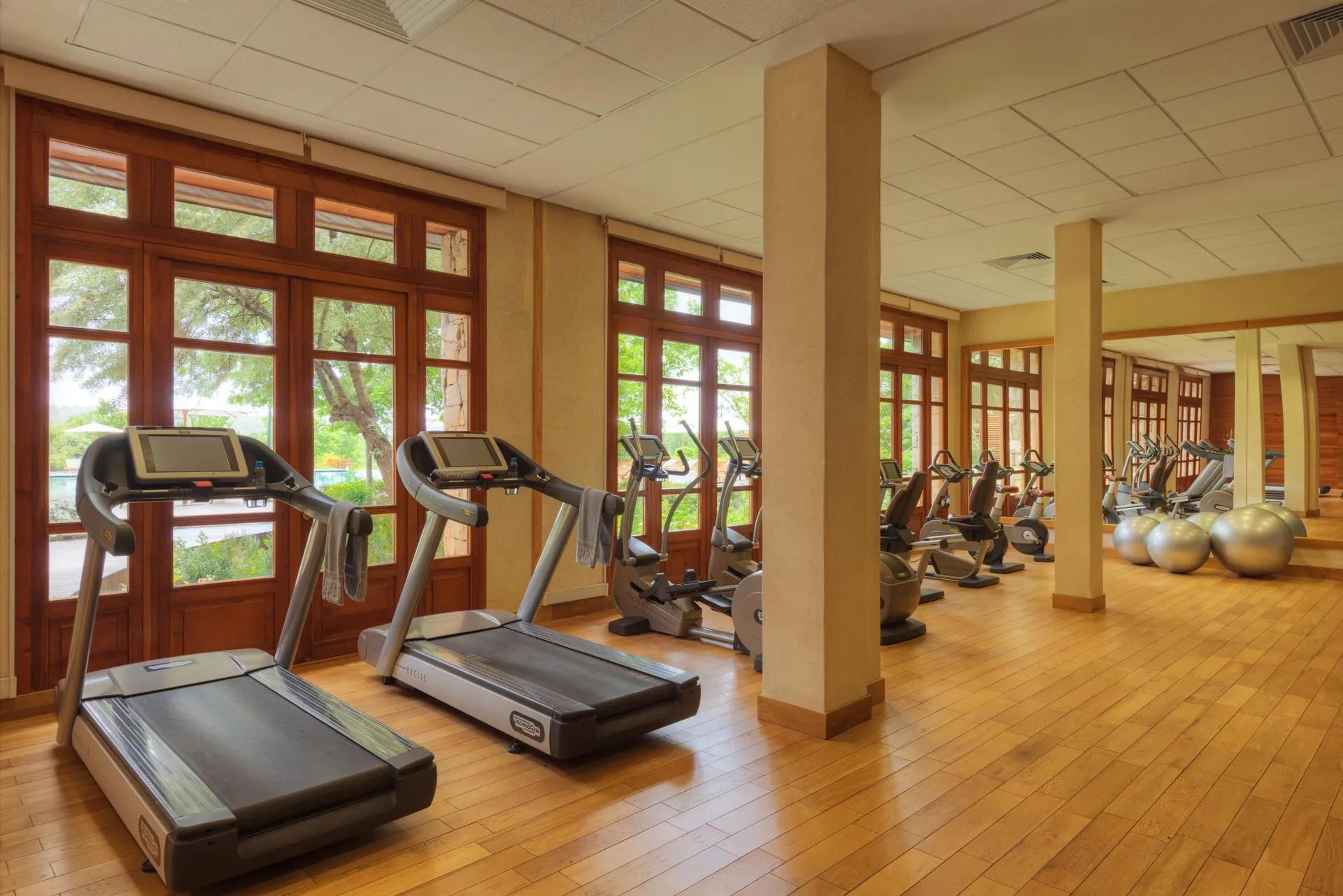 Gym with several treadmills and exercise bikes in front of large wooden windows
