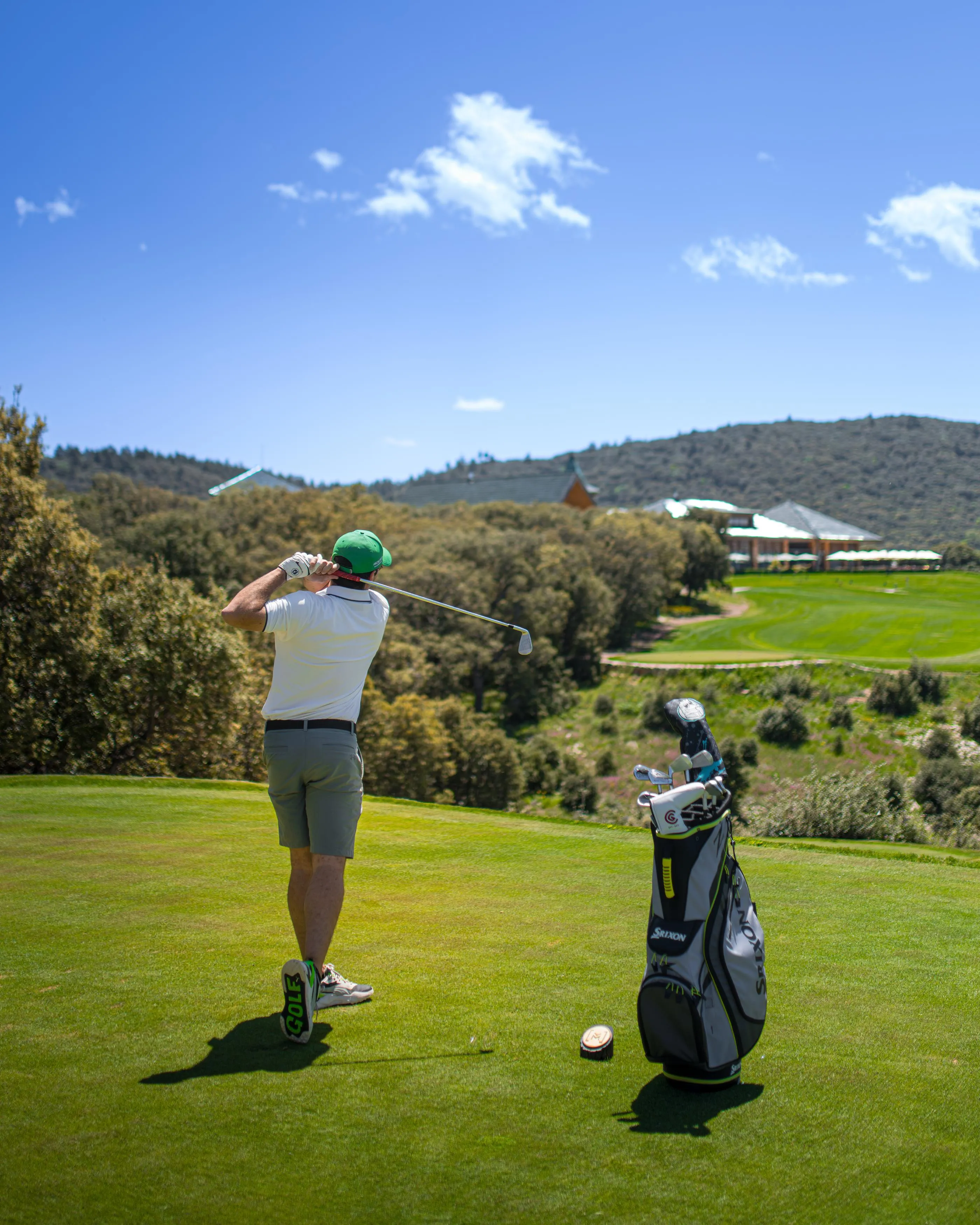A golfer hitting a ball on a golf course with a bag of clubs nearby
