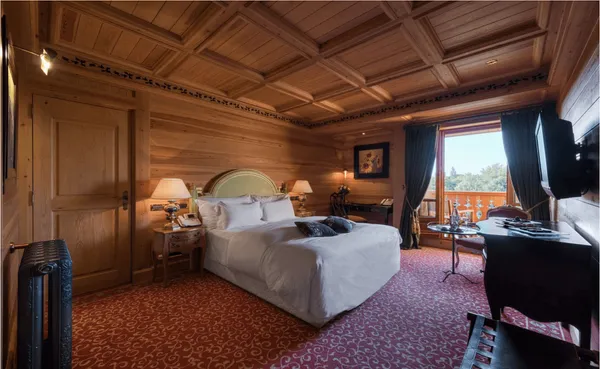 Wooden room with a double bed, bedside tables, a desk, open curtains, and an outdoor view.