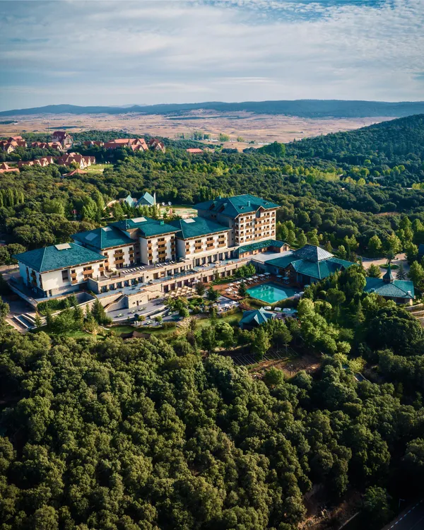 A large hotel complex surrounded by dense forest with pools and green-roofed buildings, seen from the air.