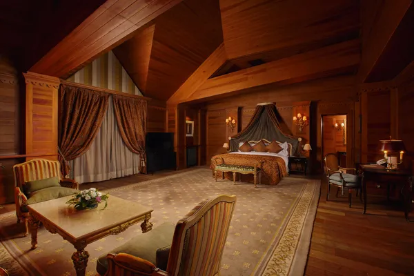 Luxurious wooden room with a large four-poster bed, sofas, a table, and lamps.