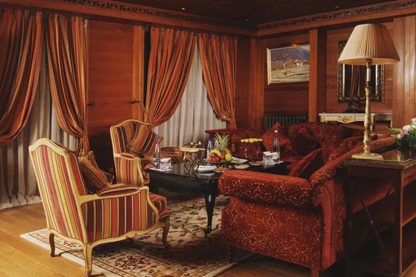 Salon avec des meubles en bois, des fauteuils à rayures et un canapé en velours rouge, décoré de coussins et de tables basses avec des fruits et des boissons