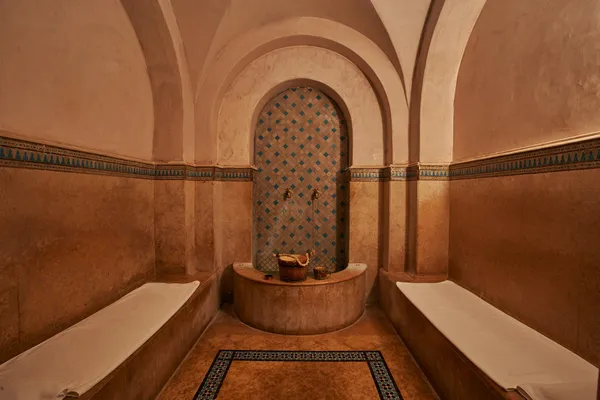 Hammam room with stone benches, a tiled niche with geometric patterns, and metal buckets