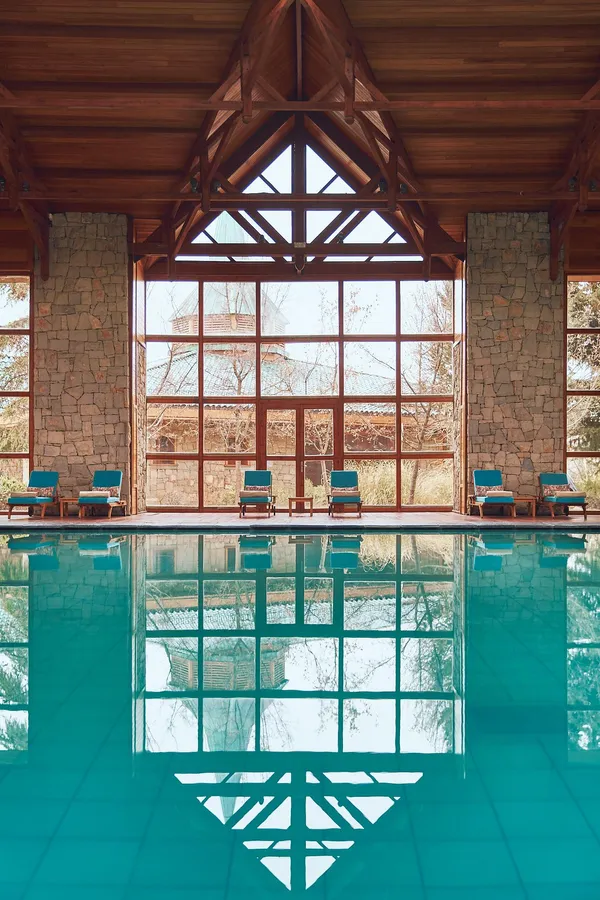 Indoor pool with a view of windows and lounge chairs through a large glass wall