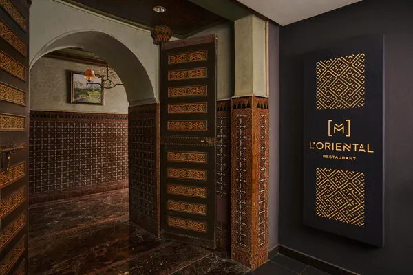 Entrée d'un restaurant nommé L'Oriental avec une porte en bois sculpté et un panneau lumineux à motifs géométriques