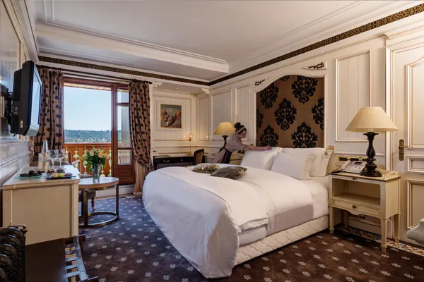 Luxurious hotel room with a double bed, a window offering a view of a landscape, bedside tables with lamps, and a wall-mounted television.