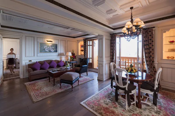 Living room with sofa, armchairs, coffee table, dining table and chandelier, a person walks through a door with a sheet