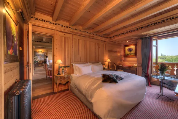 Wooden room with a large bed, a bedside table, an open window and an outdoor view.