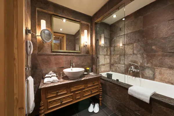 Bathroom with sink, mirror, bathtub, and towels, stone walls and wall lighting.