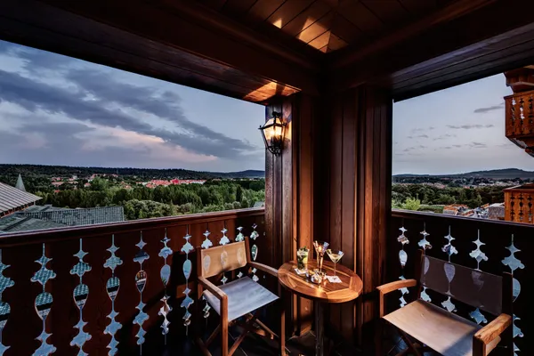 Wooden balcony with table, chairs, and glasses, offering a panoramic view of a city and hills under a cloudy sky.