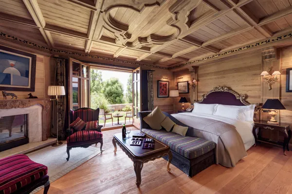 Wooden room with bed, sofa, coffee table, fireplace and French doors opening onto an outdoor terrace.