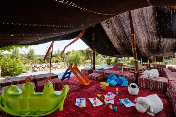 Un espace couvert avec des jouets pour enfants, des coussins et des décorations colorées, entouré de végétation
