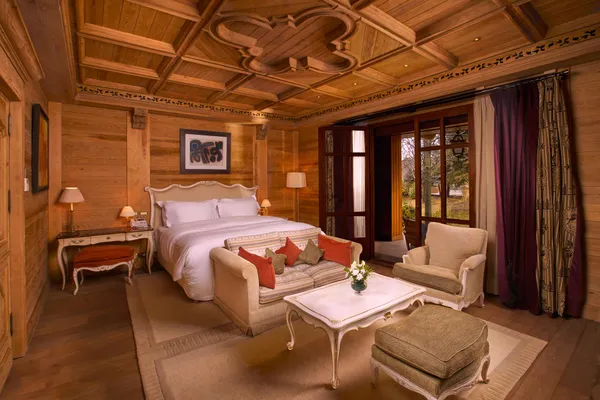 Wooden room with double bed, sofa, armchairs, coffee table and windows overlooking the outside.