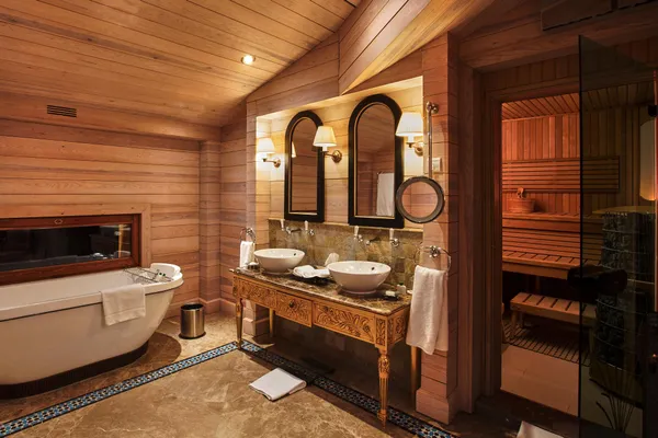 Wooden bathroom with bathtub, double sink, mirror, and open door to a sauna.