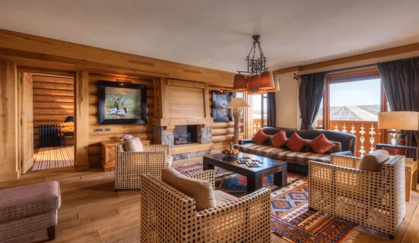 Wooden living room with sofa, rattan armchairs, coffee table, fireplace and large windows.